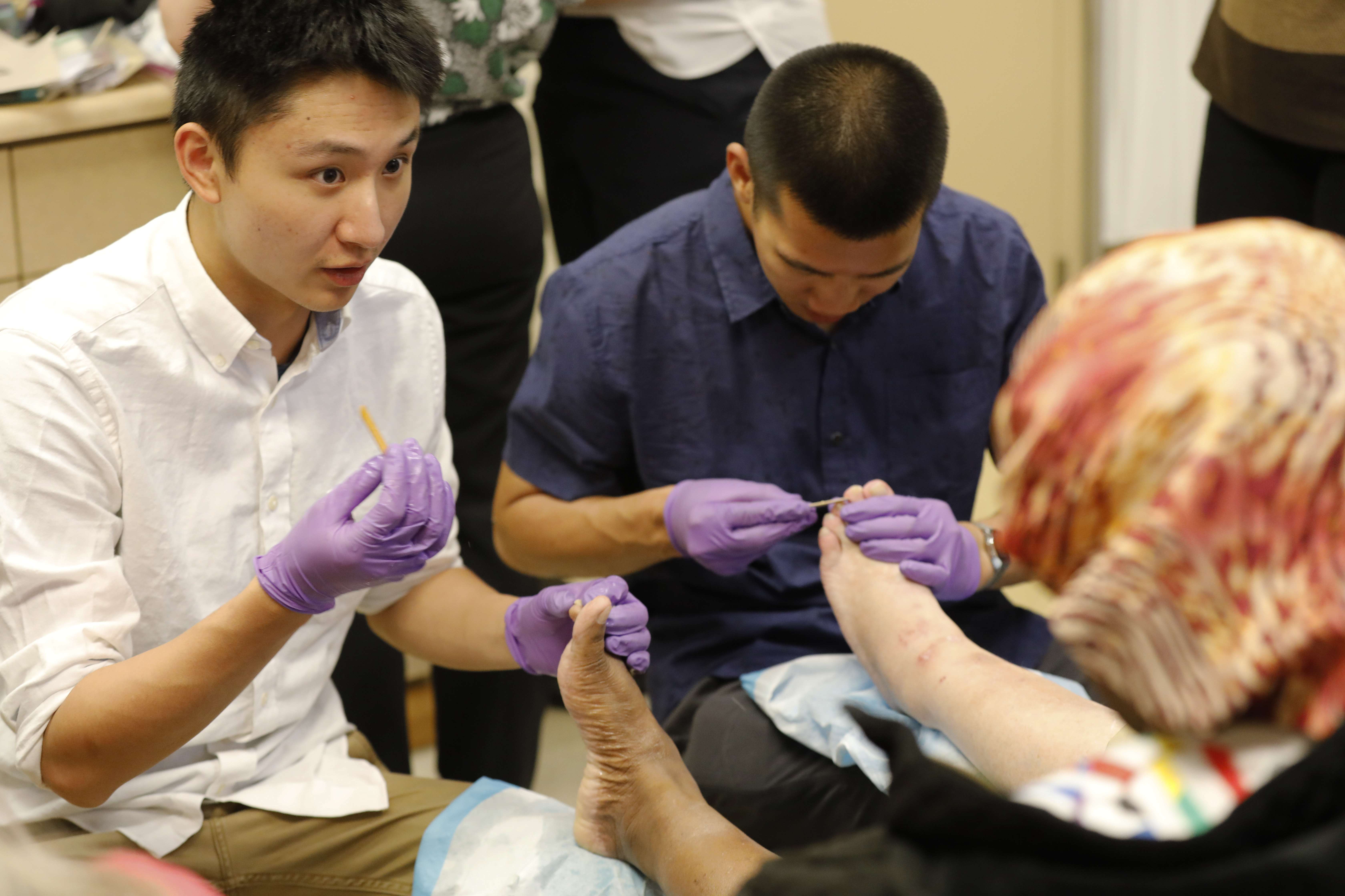 two students in gloves providing foot care to a patient